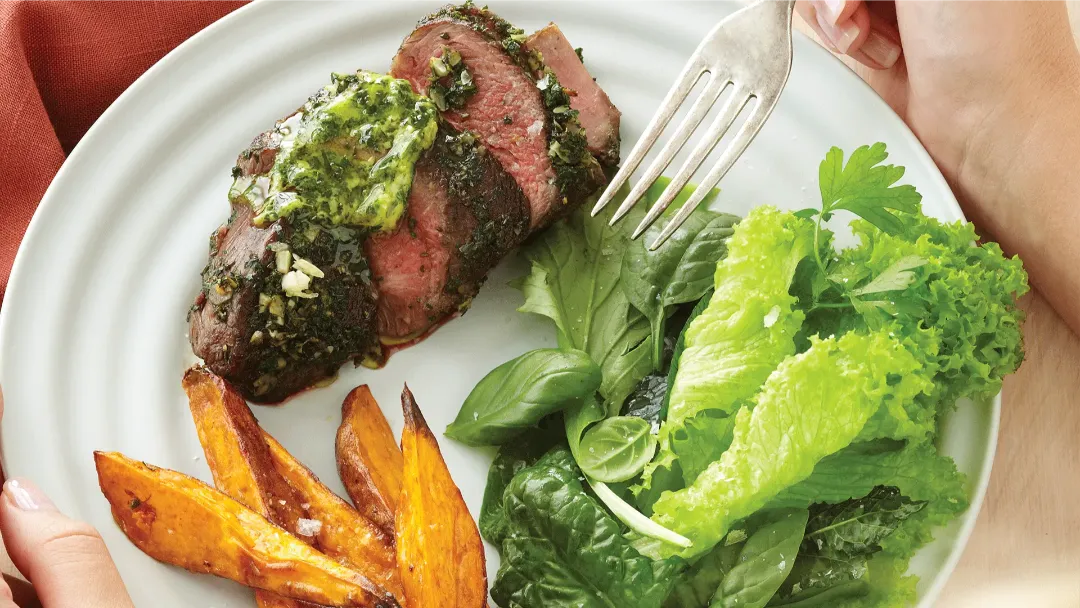 roast lamb rump on a plate served with kumara chips and a green side salad